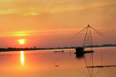 Silhouette sailboats in sea against orange sky