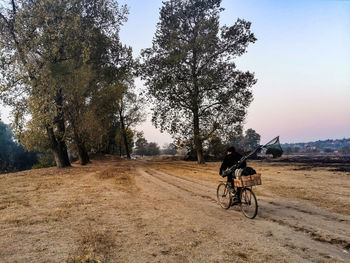 Man riding bicycle on field against sky