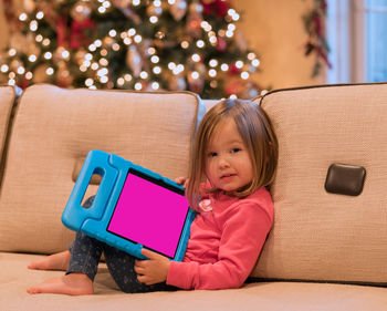 Girl using digital tablet while sitting on sofa at home during christmas