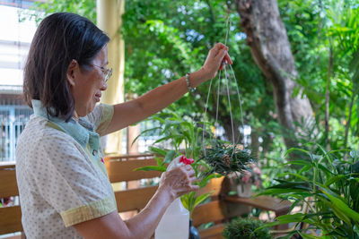 Portrait of senior retired woman watering plants in garden during free time