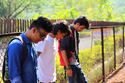 Friends looking down while sanding by fence