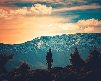 Silhouette mid adult man standing on mountain against cloudy sky during sunset