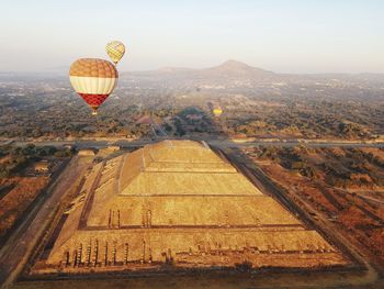 View of hot air balloon flying over landscape and ancient pyramid