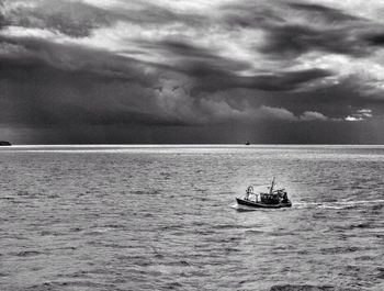 Boat sailing in sea against cloudy sky