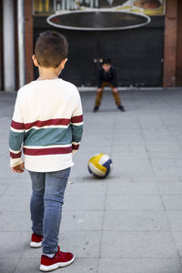 Friends playing with soccer ball on footpath