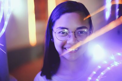 Portrait of smiling young woman amidst illuminated lighting equipment