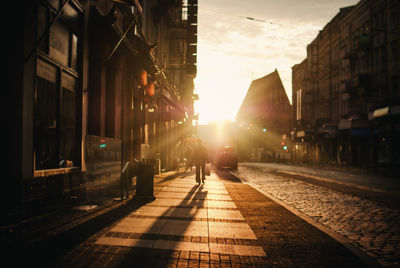 Silhouette person walking on sidewalk in city during sunset