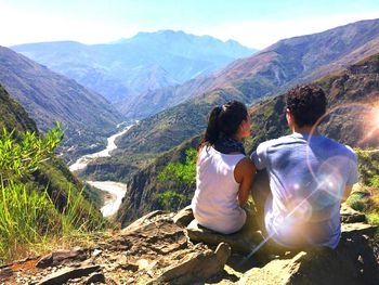 Rear view of couple sitting on mountain during sunny day