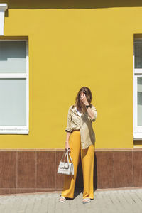 Full length of woman standing against yellow wall