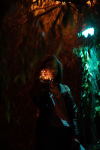 Portrait of young woman holding illuminated string lights at night