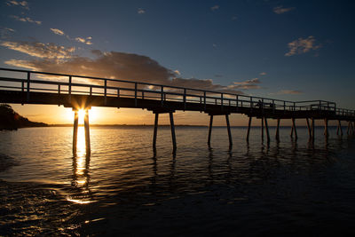 Silhouette bridge over sea against sky during sunset