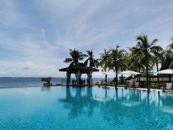 Palm trees by swimming pool against sky