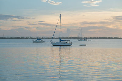 Sailboats moored on sea against sky during sunset