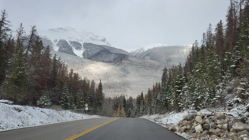 Road by snowcapped mountains against sky during winter