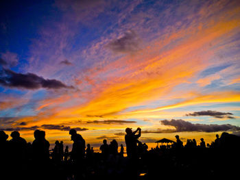 Silhouette people at beach against dramatic sky during sunset