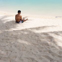 Rear view of shirtless man sitting on sand at beach