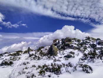 Snow covered rocks with low clouds and hiker against sky