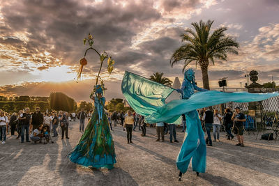 People by palm trees against sky during sunset