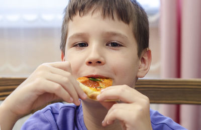 Boy eating pizza. child closed his eyes in pleasure and takes a bite of pizza piece holding it aloft