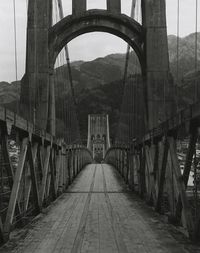 Footbridge by suspension bridge against sky