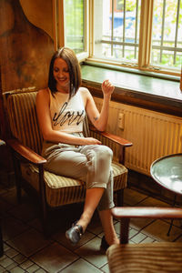 Smiling young woman sitting on chair by window