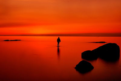 Rear view of woman standing on beach against sky during sunset