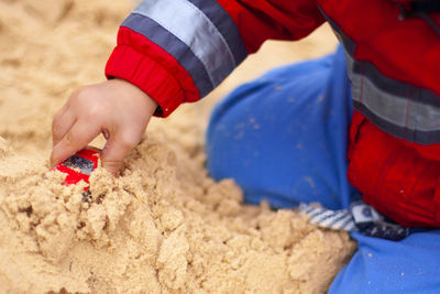 Midsection of boy playing with toy car on sand at beach