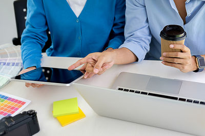 Midsection of businesswomen discussing over digital tablet at desk in office