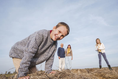 Happy boy crouching at hay bale while family in background