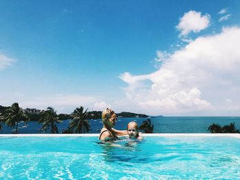 Woman with daughter swimming in pool by sea against cloudy sky