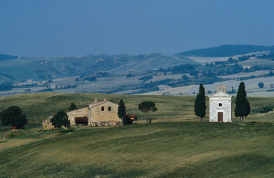Houses ane chappel on field by mountains against clear sky