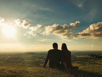 Rear view of couple sitting on field against sky during sunset