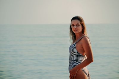 Portrait of young woman standing in sea against sky