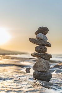 Stack of pebbles at beach against clear sky during sunset