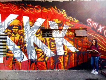 Full length of woman standing against graffiti wall