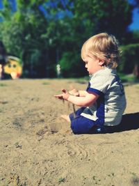 Side view of boy sitting on sand at playground