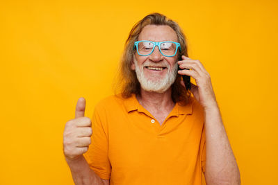 Portrait of senior man gesturing against yellow background
