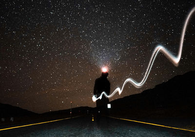 Man on illuminated street light against sky at night