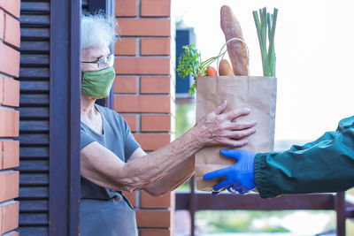 Midsection of senior woman wearing mask receiving parcel at doorstep