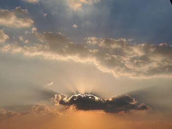 Low angle view of sunlight streaming through clouds
