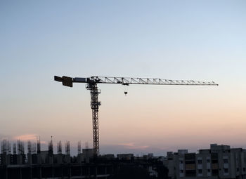 Low angle view of silhouette crane by building against sky during sunset