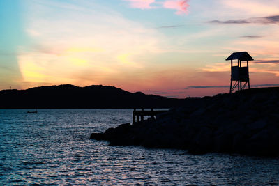 Silhouette built structure by sea against sky during sunset