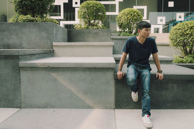 Full length of young woman sitting on retaining wall against building