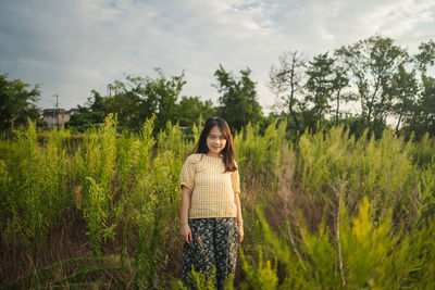 Portrait of woman standing by plants against sky