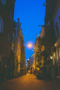 Illuminated street amidst buildings against sky at night
