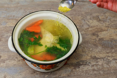 Cropped hand adding ingredient in soup bowl