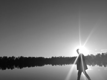 Side view of silhouette man standing by lake against sky