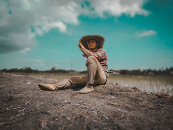 Side view of man sitting on land against sky