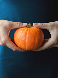 Close-up of hand holding pumpkin against orange background