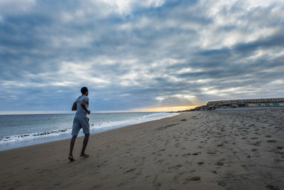 Full length of man running at beach against cloudy sky